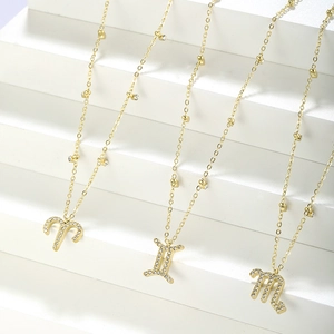 Detailed shot of three gold-plated zodiac necklaces with cubic zirconia on white steps