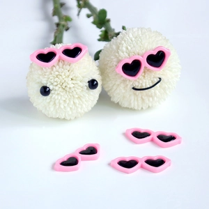 Close-up of pink heart-shaped mini sunglasses on white flowers for DIY crafts