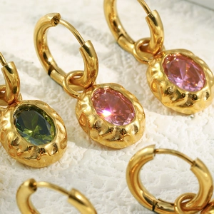 Gold hammered hoop earrings featuring pink and green oval cut crystals on sand background