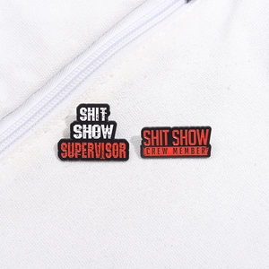 Detail of enamel pins featuring Shit Show Supervisor and Crew Member text on canvas