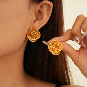 Detail view of 3D rose flower stud earrings with a matte metallic gold finish on a model