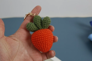 Detailed close-up of handmade orange crochet carrot keychain with green leaves and metal ring