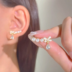 Detail of elegant pearl drop earrings with bow design and teardrop zircon on a golden base