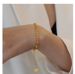 Detail of gold phoenix tail chain bracelet with heart charm on a model wrist