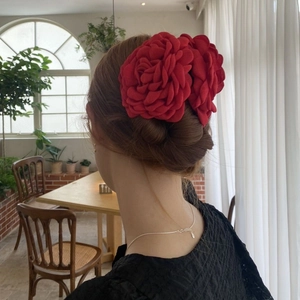 Dettaglio di una persona che indossa due grandi fermagli per capelli a fiore rosso vivo