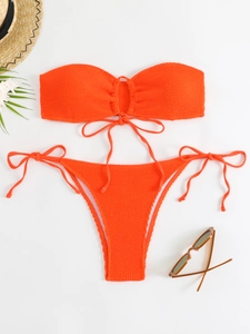 Flat lay of textured orange bandeau bikini with side-tie bottoms and summer props