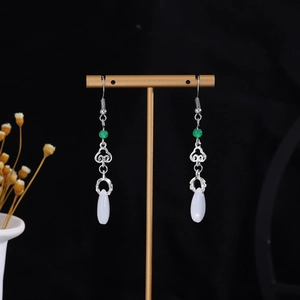 Detail of silver long drop earrings with green beads and white waterdrop pearls on a stand