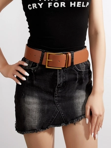 Dettaglio di una cintura larga in pelle marrone con fibbia dorata su gonna di jeans