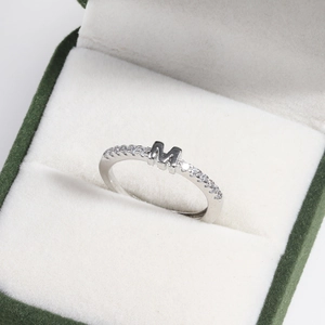 Macro detail of silver ring with letter M design and pavé stones in a premium jewelry box