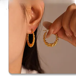 Detail of twisted 18K gold plated C-hoop earrings featuring small heart charms