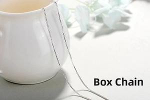 Detail of silver box chain necklace with square links draped over white porcelain