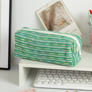Close-up of green tweed pencil case with colorful woven stripes on a tidy white desk