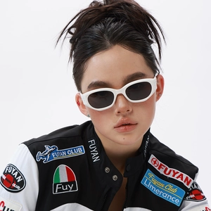 Close-up of white oval cat-eye sunglasses on a model wearing a racing style jacket