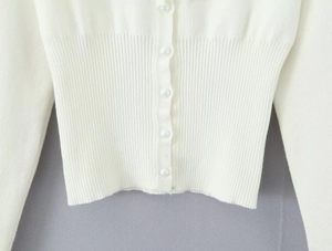 Dettaglio del cardigan bianco a maglia con vita a costine e bottoni perlati