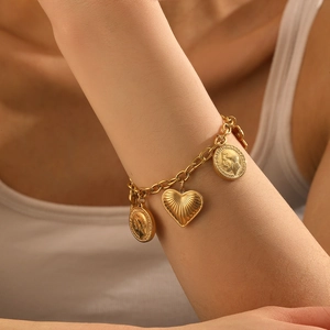 Détail d'un bracelet vintage en chaîne dorée avec pendentifs cœur et pièces au poignet