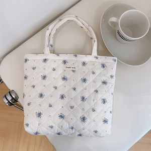 Detail of blue floral quilted cotton bag with simple wish label on white surface