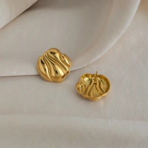 Gros plan détaillé de boucles d'oreilles dorées à texture ondulée sur tissu beige