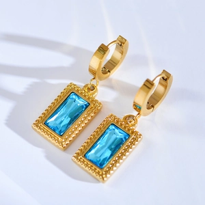 Macro view of blue emerald-cut gemstone drop earrings with golden stainless steel hoop