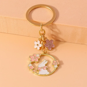 Close-up of golden metal bunny and cherry blossom keychain on textured surface