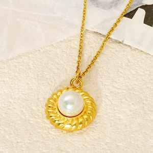Collier en acier titane doré avec pendentif perle ronde sur une surface beige texturée