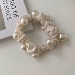 Gros plan du chouchou en satin crème avec de grandes perles brillantes sur les plis du tissu