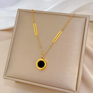 Minimalist gold titanium necklace with Roman numerals and black shell pendant on jewelry box