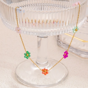 Macro view of gold stainless steel necklace with colorful beaded flowers on glassware