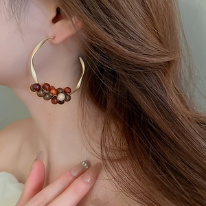 Macro side view of C-shaped golden hoop earrings with woven sandalwood beads on a model