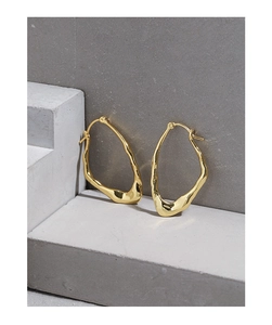 Macro shot of irregular liquid metal gold earrings with lava texture on concrete base