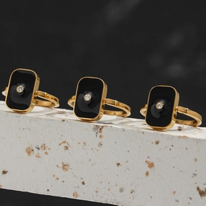 Détail de la bague dorée avec émail noir et cristal central sur un socle blanc
