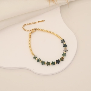 Detail of gold beaded star bracelet with natural stones on a white creative tray
