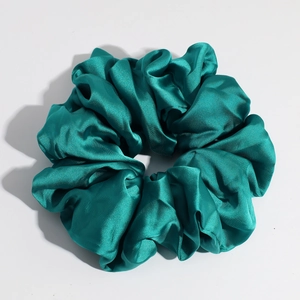 Detail view of emerald green satin scrunchie showing glossy silk texture on white surface