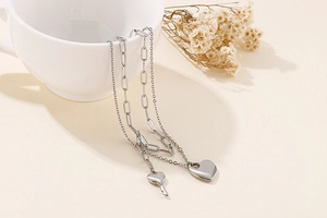 Detail of silver double-layered necklace featuring heart and key pendants on a white cup