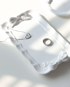 Close-up of white bow-embossed plaster tray with silver heart necklace and ring