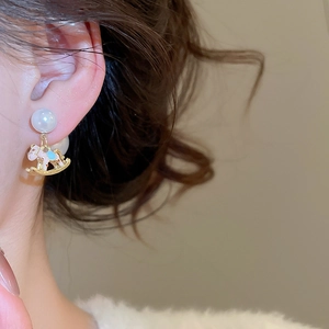 Detail of a gold rocking horse earring with colorful enamel and a white pearl on a model