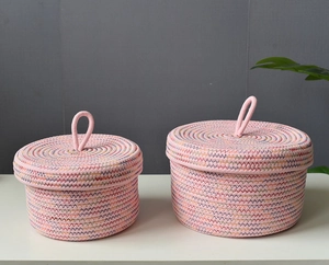 Detailed view of two pink woven cotton rope storage baskets with lids on a white desk