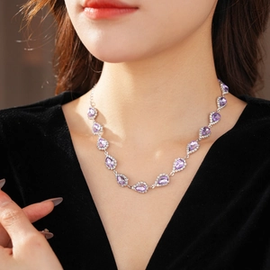 Close-up of a silver necklace featuring a purple pear-cut gemstone and clear diamonds