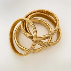 Detailed view of four stacked golden snake-bone textured elastic spring bracelets