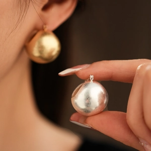 Detailed close-up of textured gold and silver sphere hoop earrings on model