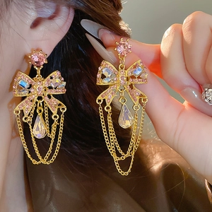 Detail of gold bow earrings with pink rhinestones and elegant fringe tassels on model