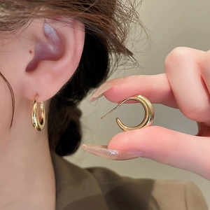 Close-up of golden C-shaped hoop earrings showing metallic shine and ear pin details