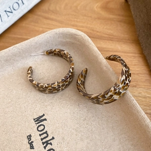 Close-up of C-shaped acetate hoop earrings with brown tortoiseshell pattern and silver pins