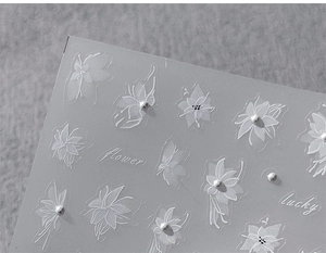Macro shot of 3D embossed nail stickers featuring white flowers and pearl accents