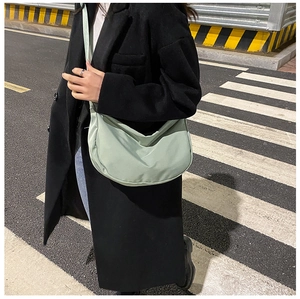 Detail of light green crescent nylon bag worn with black coat in street setting