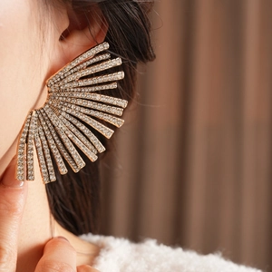 Close-up of fan-shaped geometric gold stud earrings with sparkling crystals worn on ear