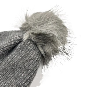 Detailed close-up of a thick grey knit beanie with a fluffy multi-tone faux fur pom-pom
