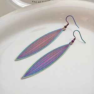 Macro detail of iridescent feather leaf earrings with textured metallic finish on tray