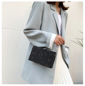 Detail of black glitter box clutch with gold star sequins and silver chain strap