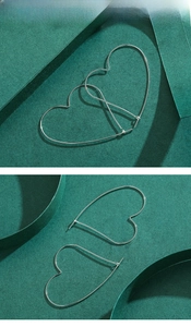 Detailed view of large silver heart-shaped hoop earrings on green textured paper background