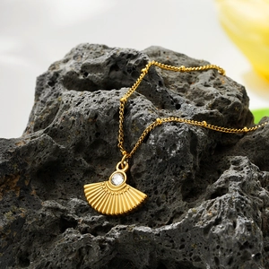 Detailed macro of gold fan pendant necklace with zircon stone on black lava rock